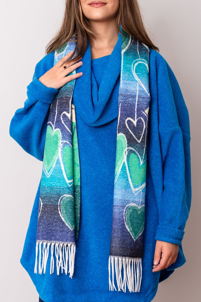 Woman wearing a blue sweater and scarf with heart patterns on a plain background